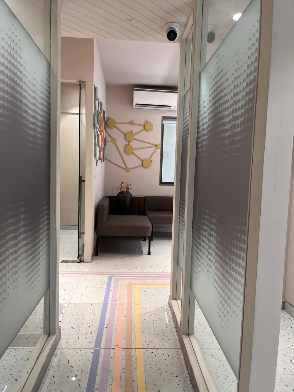 Frosted-glass corridor with colorful floor stripes leading to a lounge area